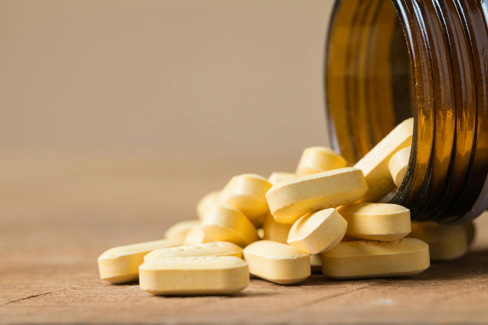 Vitamin tablets spilling from a brown bottle onto a wooden surface — a reminder that from October to March in the UK, supplementation is the practical fix for low Vitamin D.