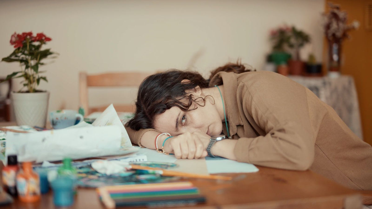 Tired woman resting her head on her hand at a desk, representing the fatigue that can come with low iron stores.