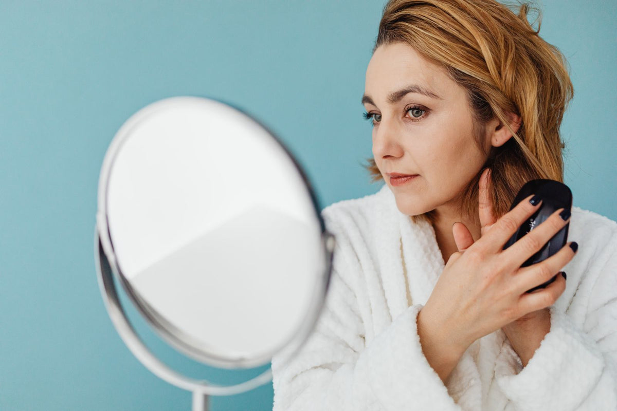 Woman looking closely at her reflection in a bathroom mirror, checking her skin.
